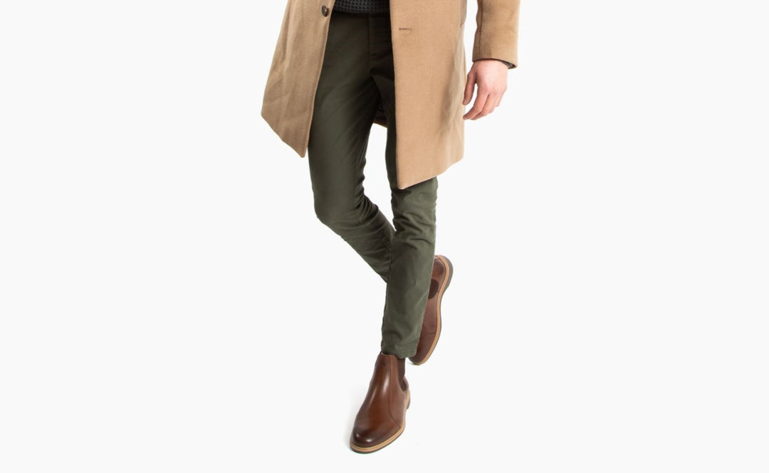 A man in chelsea boots men outfit with olive green pants and a camel peacoat